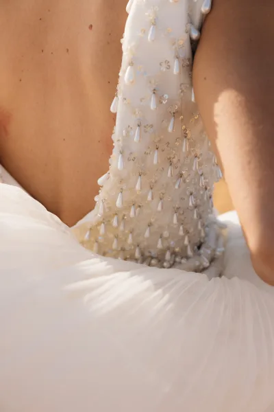 Wedding dress detail with beaded wedding dress bodice, pearl drops and sequins sparkling on the open back in warm sunlight