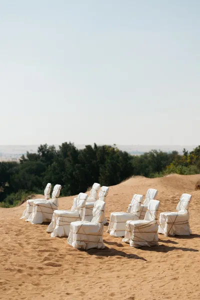 Ceremony seating with outdoor wedding chairs in white covers and rope tie backs set on sand dunes beneath open desert sky