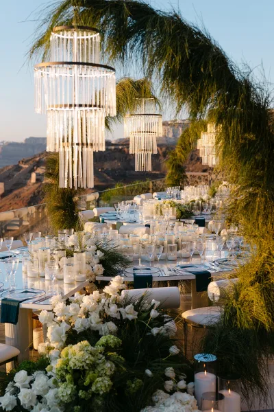 Reception tablescape styled for outdoor reception decor, framed by a greenery arch and overlooking mountains beyond a glass railing.