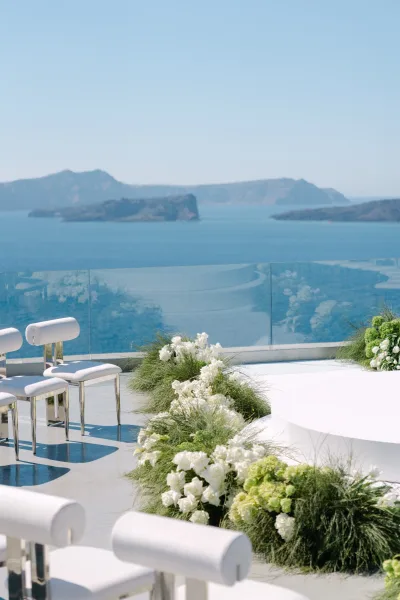 Ceremony setup showcasing outdoor ceremony decor on a round platform, framed by an ocean view terrace with glass railing and distant islands.