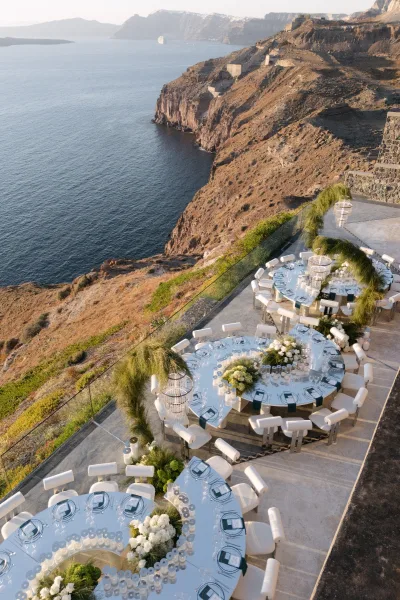 Reception tablescape showcasing elegant outdoor reception decor on a terrace with mirror tables, overlooking the ocean and cliffs.