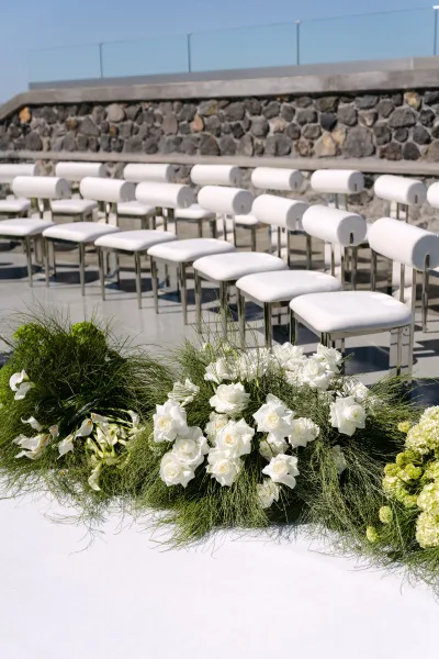 Ceremony aisle decor with white floral aisle arrangements accented by calla lilies, lining a concrete terrace framed by stone wall and glass railing.