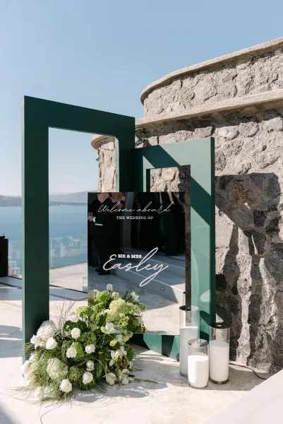 Wedding welcome sign, an acrylic welcome sign mounted on a dark green geometric frame, set against an ocean view terrace.