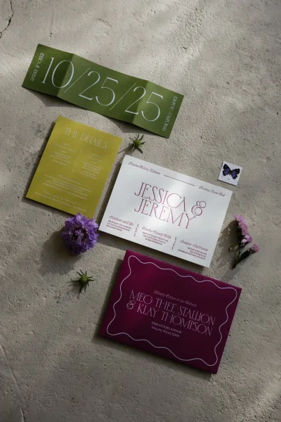 Invitation suite with modern wedding invitations, envelopes, RSVP and details cards, plus purple and dried flowers on a concrete surface