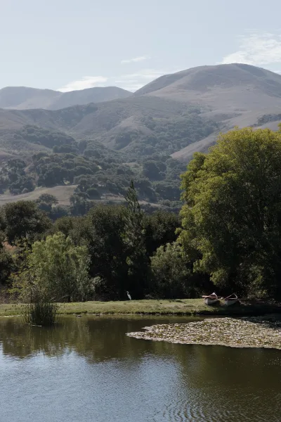 Wedding venue landscape outdoor wedding venue view with canoes on a lily pad lake, framed by trees, rolling hills, and mountain backdrop under open sky