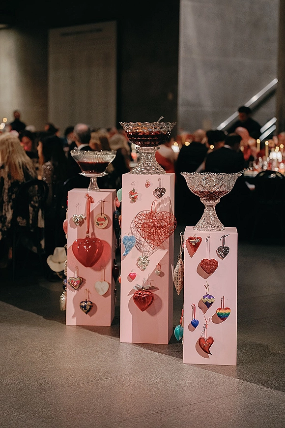 Wedding cocktail display with glass punch bowls on pink pedestals and hanging heart accents, set by candlelit banquet tables and stairs