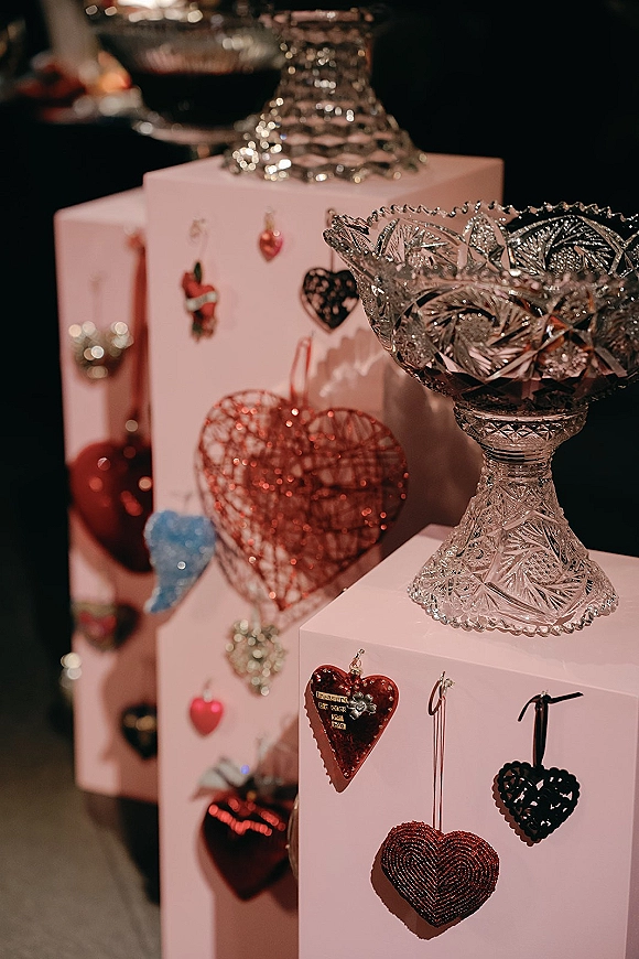 Wedding decor details with wedding cocktail hour decor on pink pedestals, heart ornaments and crystal cut glass bowls in a dark reception space