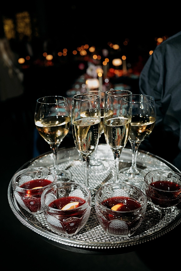 Champagne tray service with champagne flutes, white wine and red cocktails on a silver serving tray under bistro string lights in a dark reception