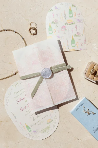 Invitation suite wedding invitation flat lay with velvet ribbon, wax seal, envelopes, RSVP card, and rings arranged on marble surface