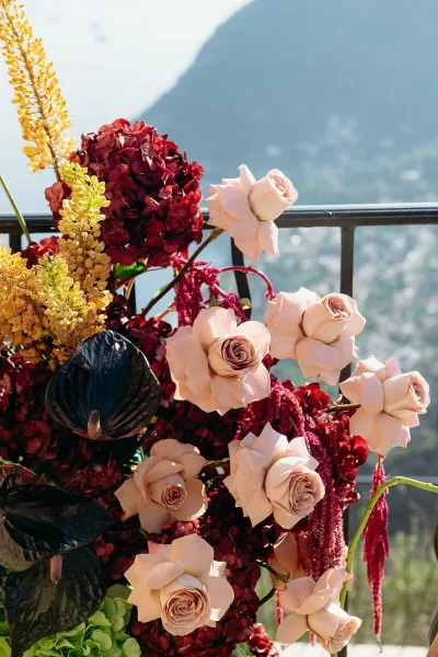 Wedding flowers on a ceremony arch with blush roses and hanging amaranthus framing a balcony railing with mountain views beyond