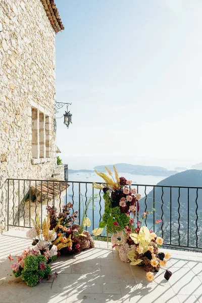 Ceremony altar decor with wedding ceremony flowers in asymmetrical floor arrangements on a terrace overlooking ocean cliffs and islands