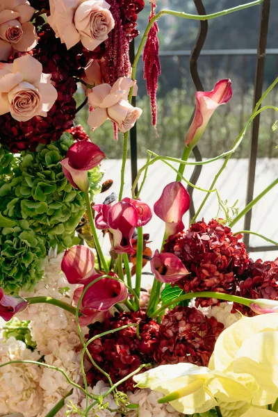 Wedding floral arrangement with ceremony altar flowers, blush roses and burgundy calla lilies on an outdoor railing with trees in daylight