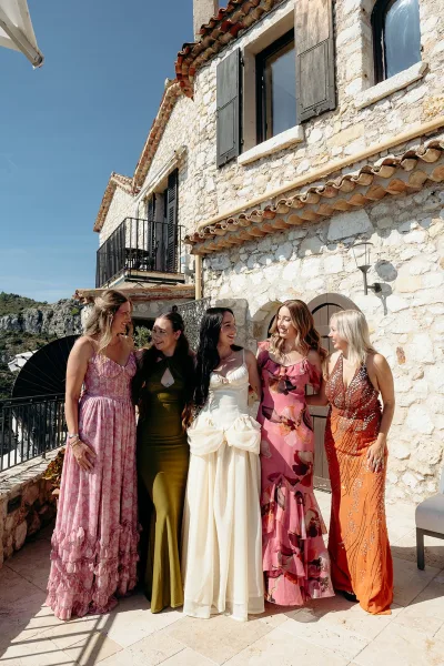 Bridesmaids portrait of the bride with bridesmaids in colorful dresses and heels on a stone villa terrace with blue sky and cliffs