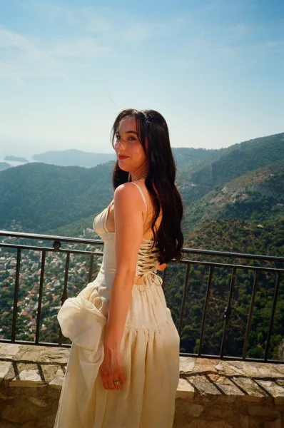Bridal portrait of a bride looking back in a spaghetti strap gown, showing lace-up corset back on a balcony with mountain valley views