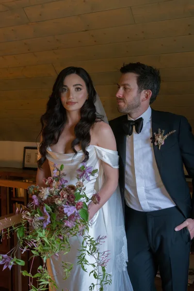 Couple portrait of groom looking at bride holding a wedding bouquet, her veil draped over an off-the-shoulder dress before wood paneling