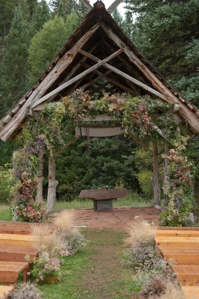 Ceremony setup for an outdoor wedding ceremony with rustic wooden altar, floral garland and wildflowers, benches on a forest grass aisle