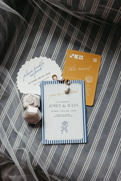 Wedding invitation suite featuring a blue and white invitation, styled with a velvet ring box on striped fabric