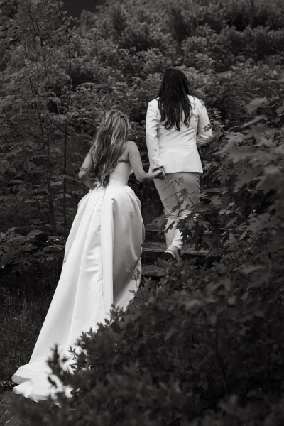 Couple portrait in an outdoor couple moment, walking up stone steps through garden foliage, her dress train trailing beside her partner.