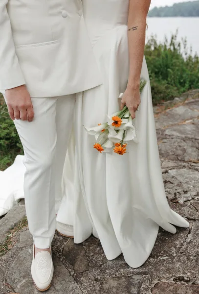 Couple portrait along a stone path by the lake, the pair holding a calla lily bridal bouquet amid lush greenery.