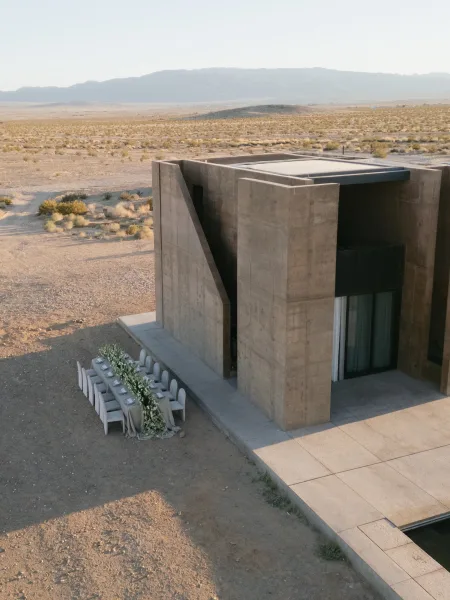 Reception tablescape set on an outdoor reception table with a lush floral runner, against a desert landscape and concrete architecture.