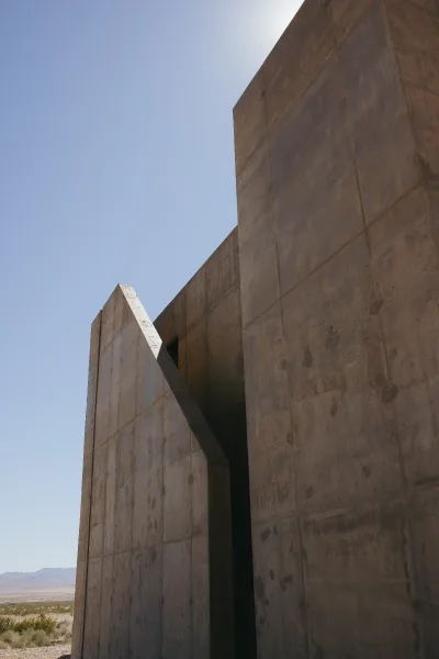 Venue exterior of a modern concrete building with an exterior staircase, set against a blue sky and desert landscape with distant mountains.
