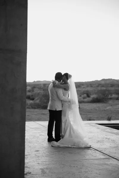 Wedding kiss portrait as a bride and groom embrace on a concrete patio facing distant hills, her bridal veil catching the open sky.