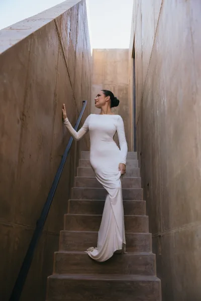Bridal portrait in a long sleeve wedding dress, posing on a concrete staircase beneath open sky, highlighted by a sleek bridal updo.