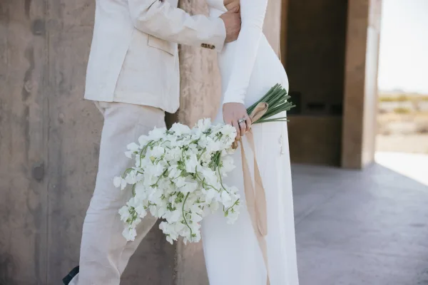 Bridal bouquet, a white wedding bouquet with trailing ribbon, held gracefully with a desert landscape softly fading in the background.