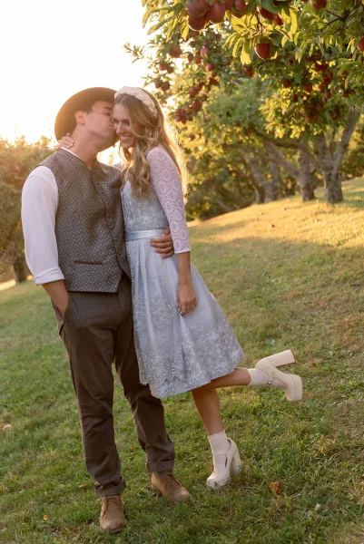 Couple portrait of bride and groom embrace with a forehead kiss, bride in lace dress and floral headband in a sunset apple orchard field