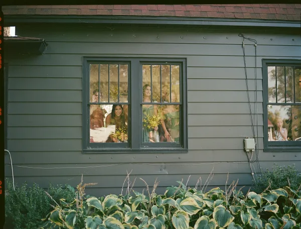 Bridesmaids portrait with bridesmaids in window, holding bouquets in rust dresses, peeking and laughing behind house glass with reflections
