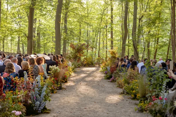 Ceremony aisle decor with wildflower ground arrangements and pampas grass lining a dirt path between wooden benches in a forest setting
