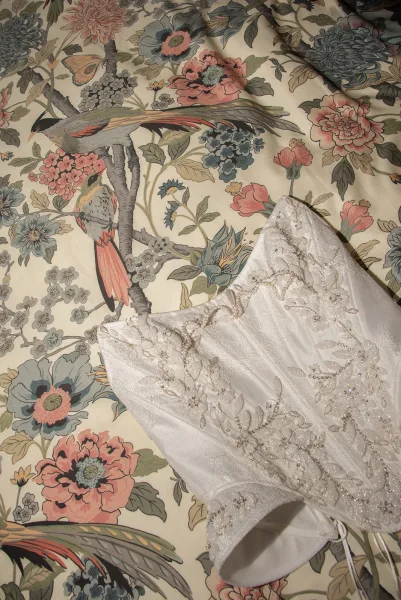 Wedding dress close-up showing a strapless lace wedding dress bodice with beaded embroidery and corset lacing on floral bird wallpaper