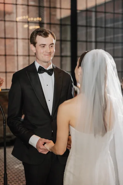 Wedding first dance as bride in veil and strapless gown holds her groom in tuxedo under a chandelier in a brick-walled loft with grid windows