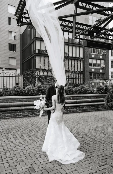 Wedding couple portrait in black and white with bride and groom embracing under a billowing cathedral veil in an urban cobblestone courtyard