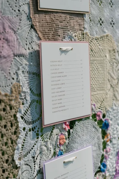 Wedding seating chart, a hanging seating chart framed with crochet doilies, neatly listing tables and names against a grass lawn