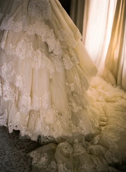Wedding dress close-up showcasing lace wedding dress detail with floral applique on a tulle skirt and long train in soft window light