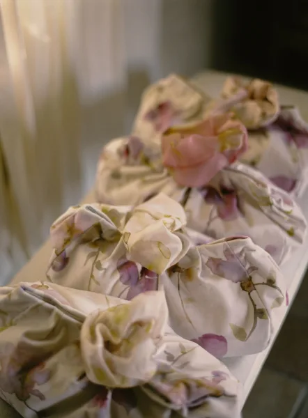Wedding favors wrapped wedding favors in floral fabric with pink ribbon accents arranged on a tabletop in an indoor room