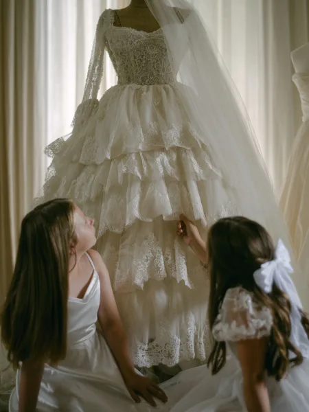 Wedding dress with lace wedding dress details on a mannequin, long sleeves and layered tulle skirt, veil draped by window light and sheer curtains