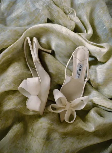 Bridal shoes, white wedding heels with satin slingback straps and bow details, arranged on softly draped fabric backdrop