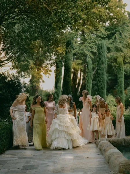 Wedding party portrait of bride with bridesmaids and flower girls in pastel dresses on a stone bridge by water with trees