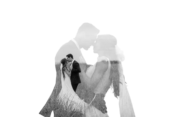 Wedding kiss portrait in a black and white wedding photo, bride in veil and gown kissing groom in suit in a tall grass field under sky