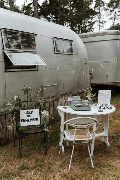 Wedding guest book with typewriter guest book cards, sign, and flowers on a table with clothespins line in a grassy outdoor setting