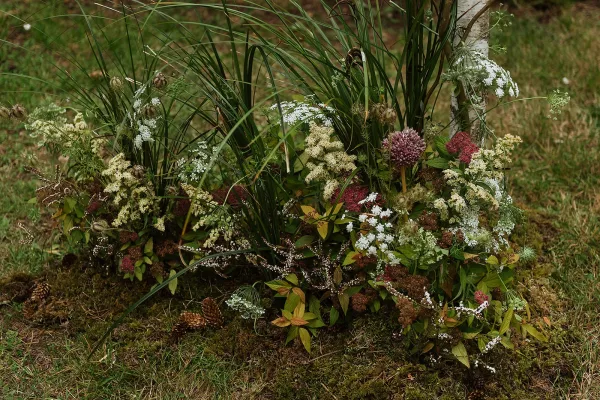 Wedding aisle flowers in a meadow-style ground floral installation with greenery, tall grasses, white and burgundy blooms beside a driftwood log