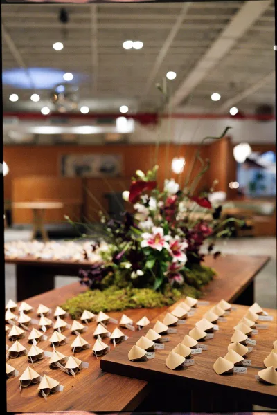 Escort card display with wooden boards holding guest name cards, set on a moss runner with floral centerpiece under soft indoor lights