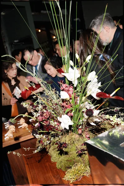 Wedding floral arrangement with a reception floral centerpiece of white blooms, anthurium, tall grasses, and moss on a wooden table with place cards