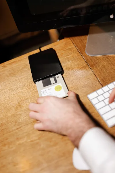 Save the date card with wedding save the date wording displayed on a computer monitor beside a floppy disk on a wooden office desk setup
