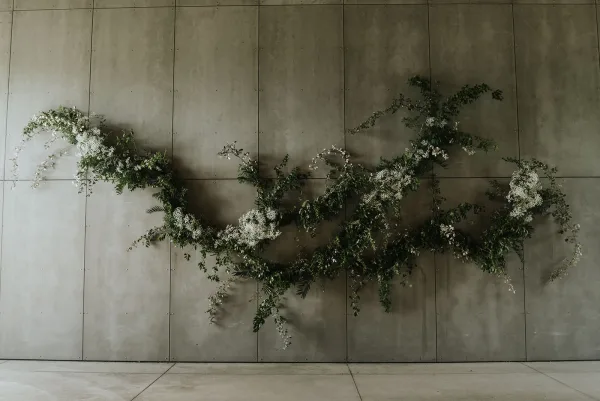 Wedding floral installation with hanging greenery installation of white flowers and trailing vines against a concrete wall backdrop