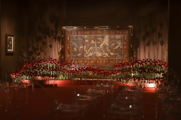 Reception tablescape with red rose tablescape bud vases, candlelit place settings and glassware against dark walls with framed artwork and uplighting