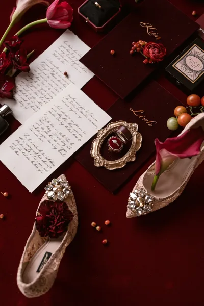 Wedding flat lay with wedding invitation suite, rings in boxes, lace bridal shoes, tulips and grapes on burgundy fabric backdrop