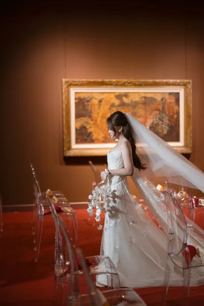 Bridal portrait of a bride in a strapless lace dress with long veil, holding a cascading orchid bouquet in a banquet room with red napkins